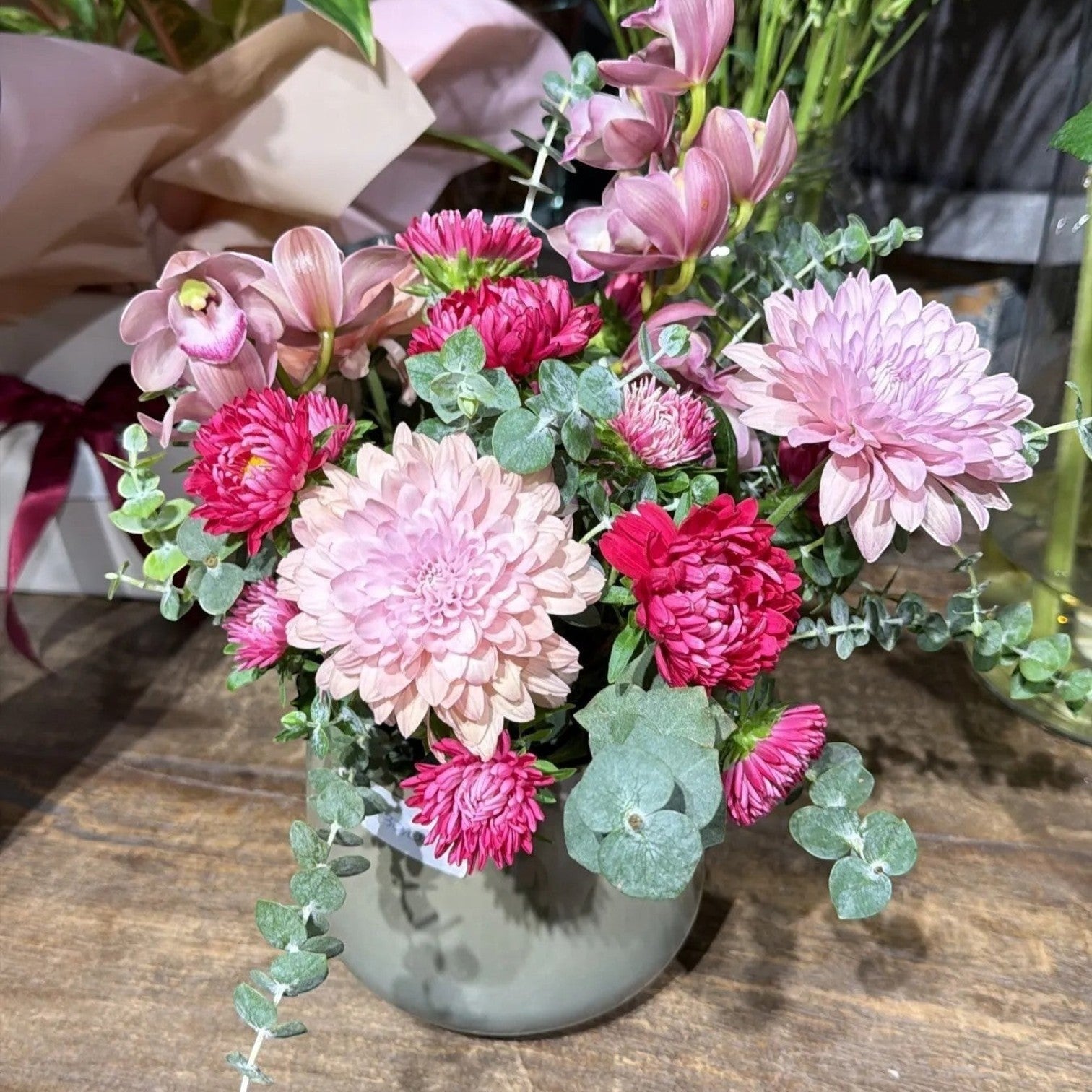 AMABILE FLOWER SHOP pink and red chrysanthemum and orchid arrangement with eucalyptus in a grey vase.